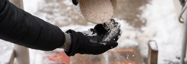 Hand streut Salz auf Schnee.