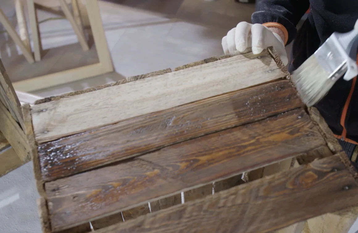 Person lasiert Holzkiste mit Pinsel