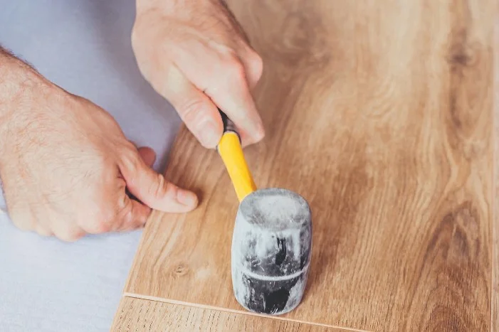 Person verlegt Holzdielen mit Gummihammer