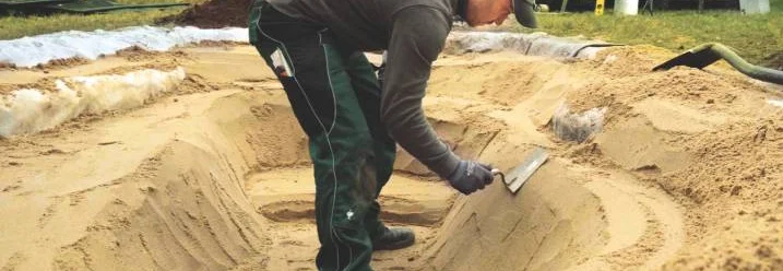 Person formt Sand mit Kelle für einen Teich