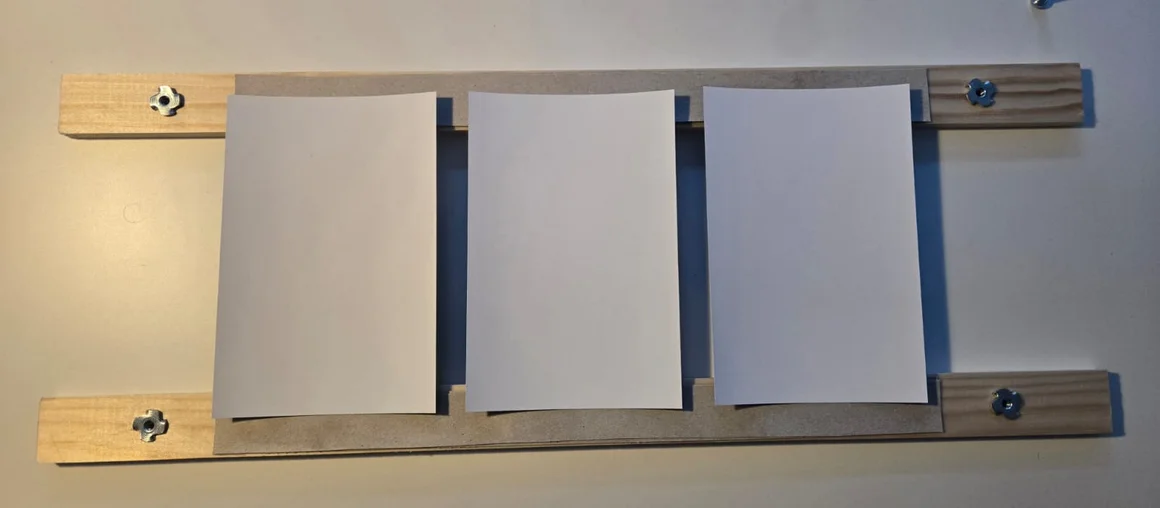 Eine hölzerne Bilderleiste mit drei weißen Blättern Papier.