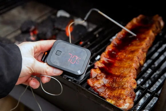 Person misst Temperatur von Rippchen auf Grill