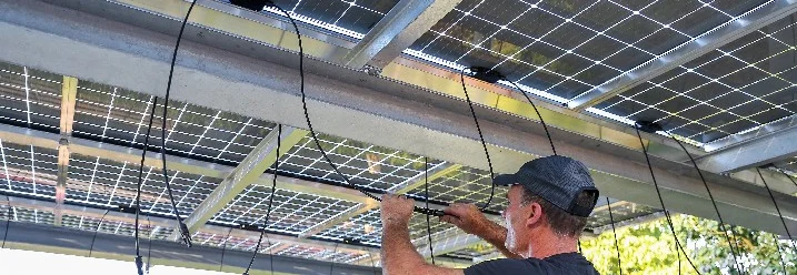 Person verkabelt Solarpanele auf einem Carport.