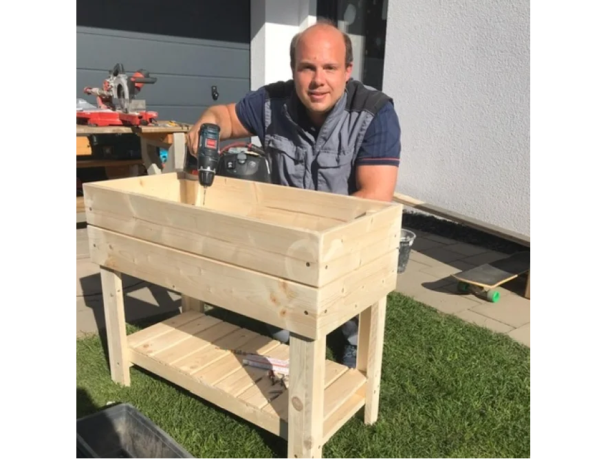 Person baut einen hölzernen Blumenkasten mit einem Akkuschrauber zusammen.