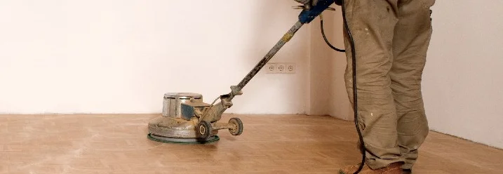 Person schleift Parkettboden mit Maschine