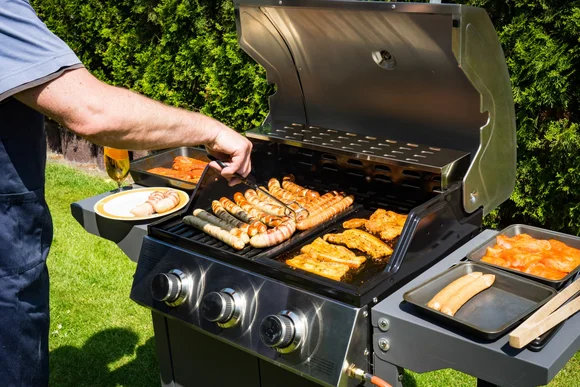 Person grillt Würstchen und Fleisch auf einem Gasgrill