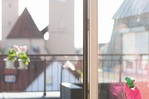Person reinigt Fenster mit Sprühflasche