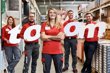 Fünf Toom Mitarbeiter in roter Arbeitskleidung halten die Buchstaben T O O M hoch