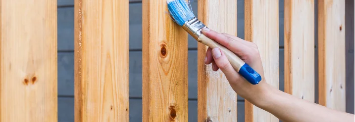 Person streicht Holzzaun mit Pinsel