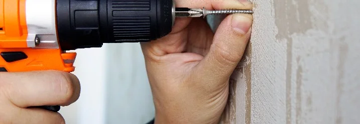 Hand benutzt Akkuschrauber an Wand