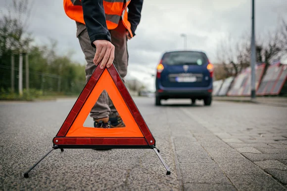 Eine Person stellt ein Warndreieck auf eine Straße
