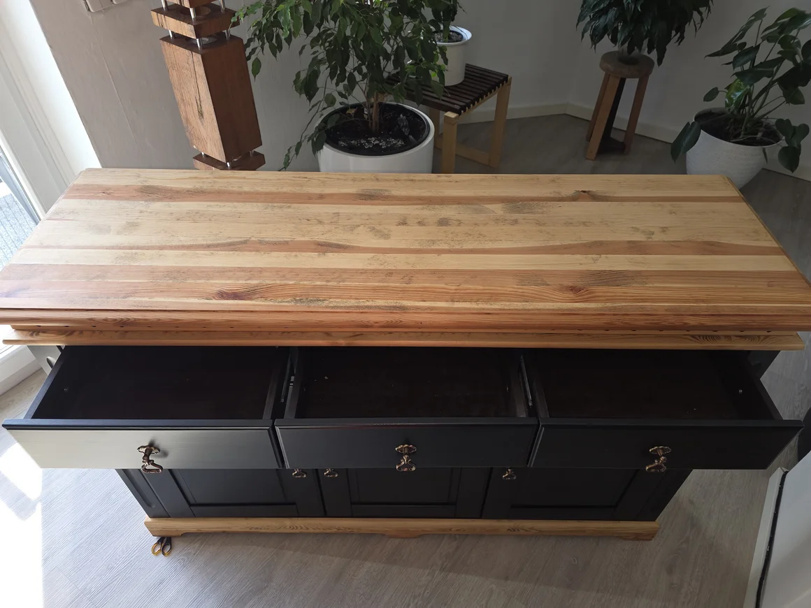 Eine schwarze Kommode mit einer Holzplatte und drei offenen Schubladen.