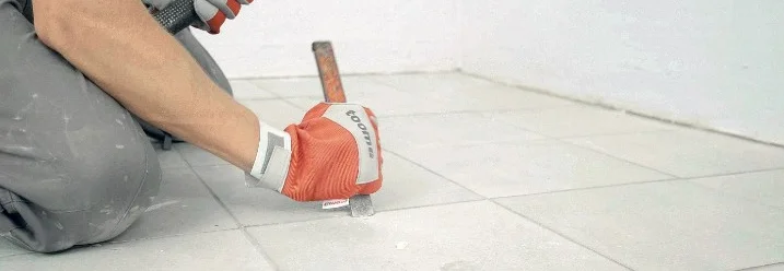 Person entfernt Fliese mit Hammer und Meißel