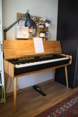 Ein digitales Klavier in einem Holzgehäuse auf einem Schreibtisch.