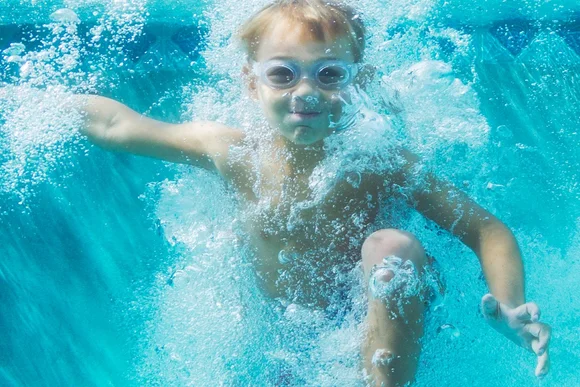 Kind mit Schwimmbrille taucht im Pool