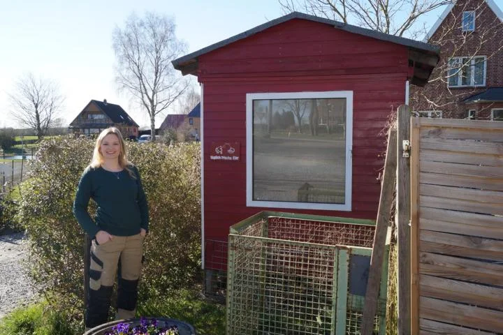 Person steht vor rotem Gartenhaus