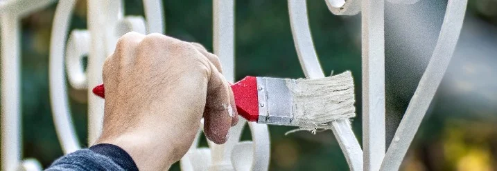 Hand streicht Metallzaun weiß