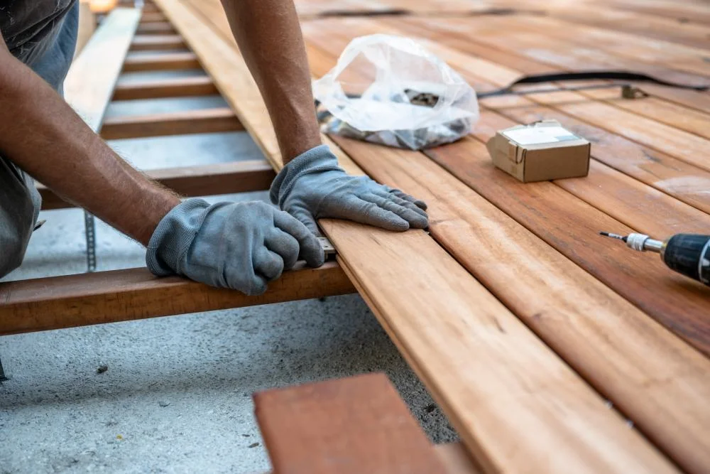Eine Person mit Arbeitshandschuhen montiert die Dielen einer Holzterrasse.