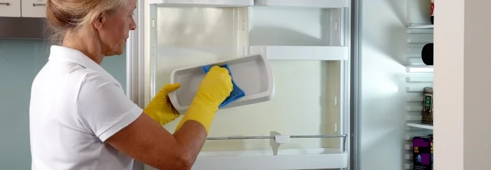 Person reinigt Kühlschrank mit Tuch
