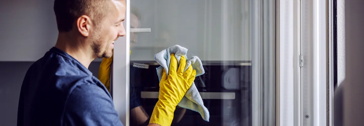 Person reinigt Fenster mit blauem Tuch