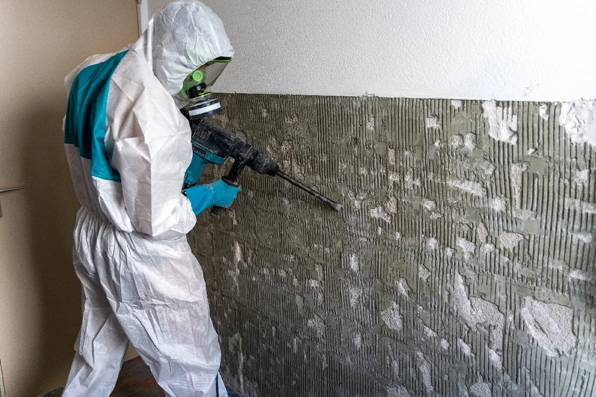 Person in Schutzkleidung entfernt Fliesenkleber mit Bohrhammer