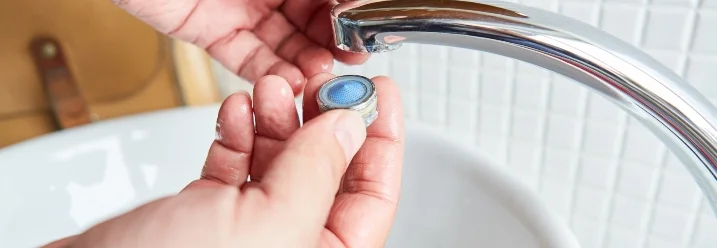 Person hält einen Wasserhahn-Sieb in der Hand.