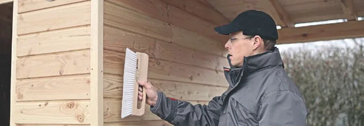 Person reinigt Gartenhauswand mit Bürste