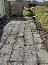 Ungepflegte Terrasse aus Waschbetonplatten mit einer Schubkarre im Hintergrund.