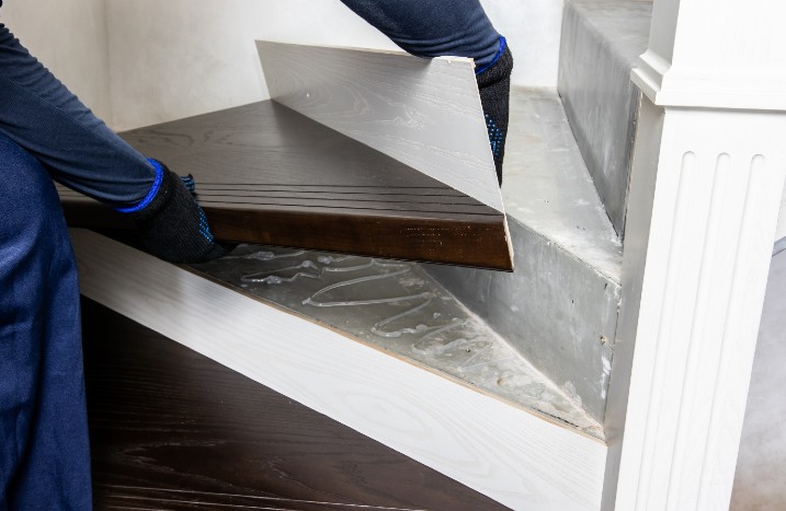 Eine Person montiert eine neue Holzstufe auf einer Betontreppe.