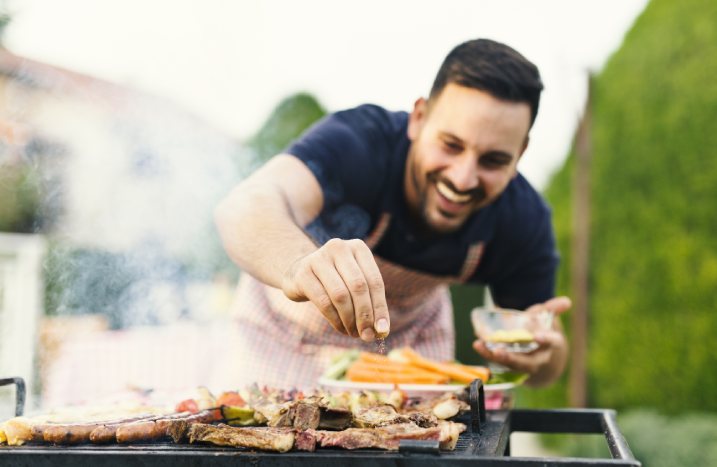 Person würzt Fleisch auf dem Grill